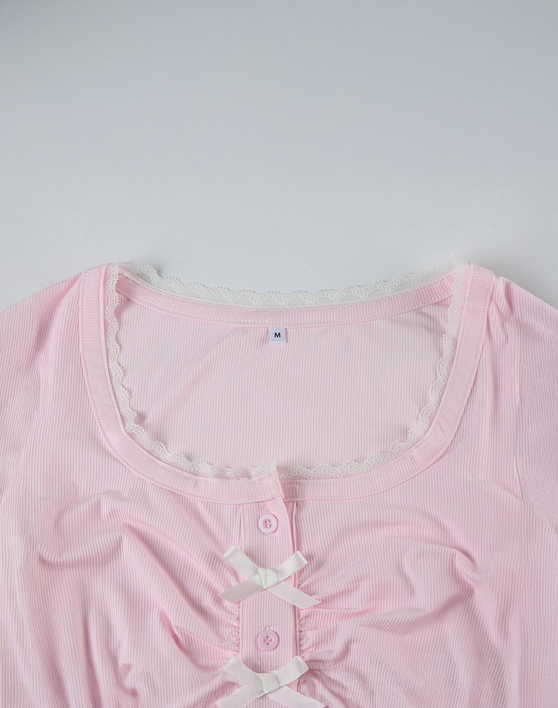 Detailed view of a pink ruched bow crop top, featuring a button front and feminine charm with dollette style details.