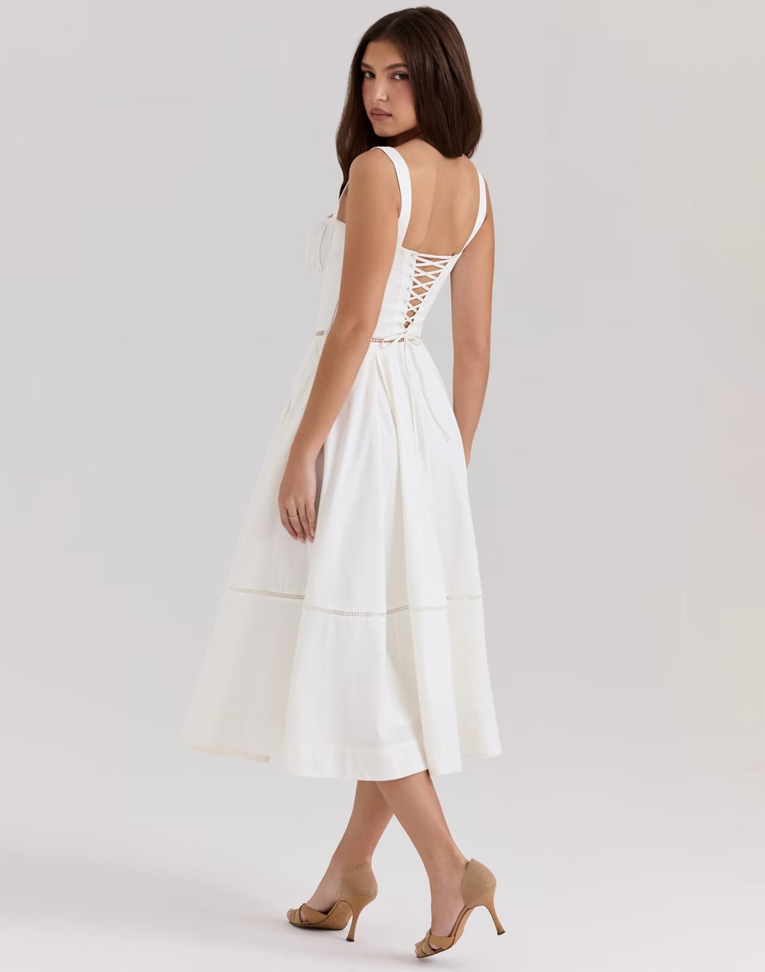model wearing white corset dress with lace-up back and flared midi skirt, styled with nude heels